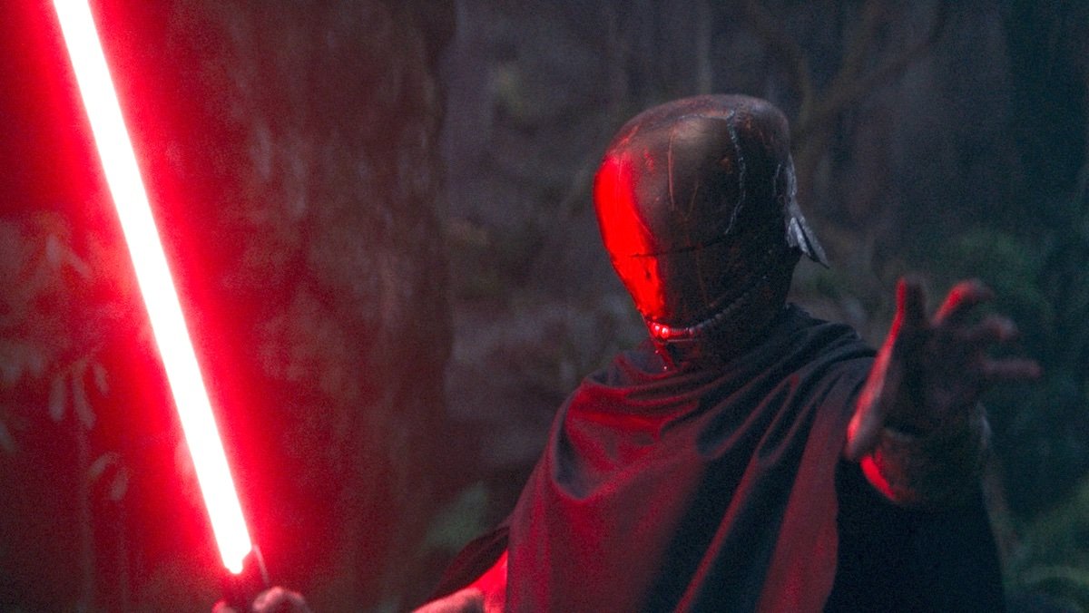 O Mestre mascarado com a mão estendida enquanto segura um sabre de luz vermelho na outra em The Acolyte