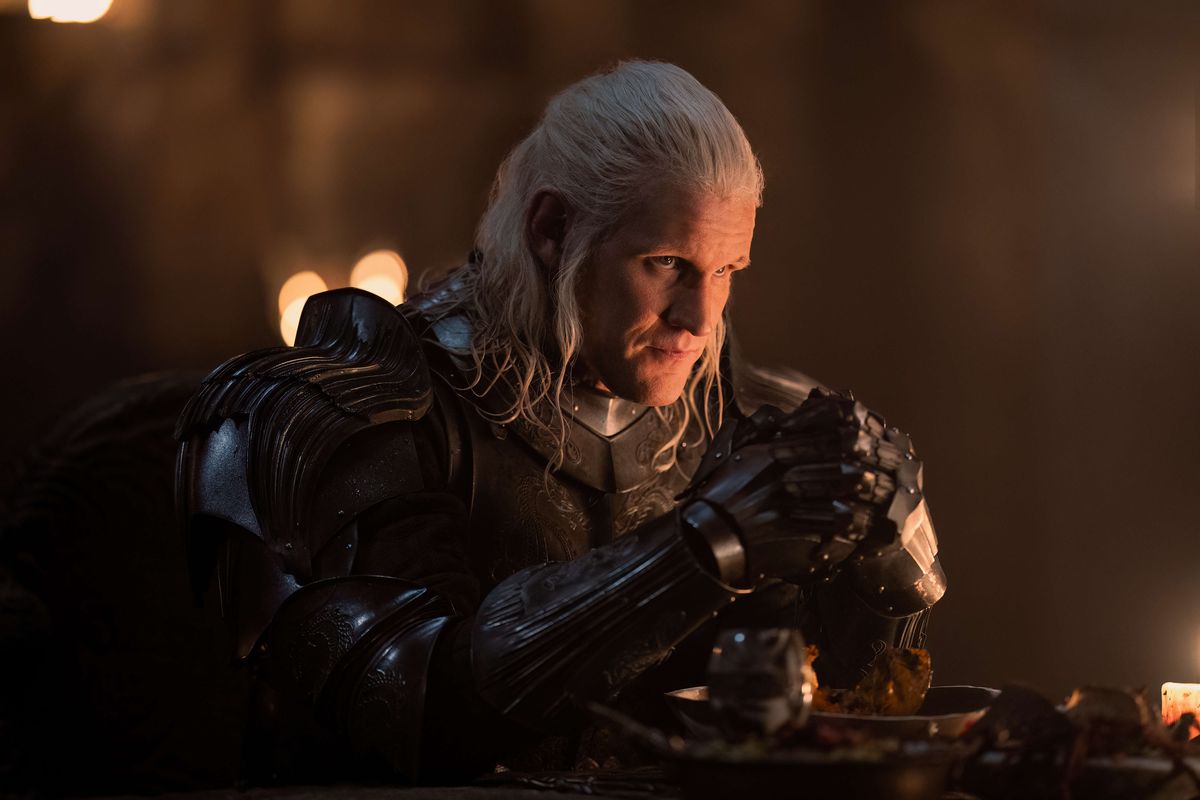 Matt Smith como Daemon Targaryen usando armadura e sentado em uma mesa em House of the Dragon