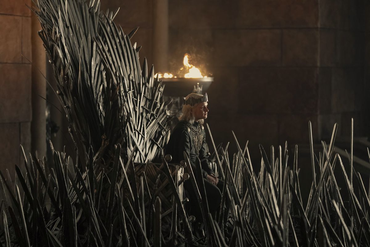 O jovem Rei Aegon está sentado no Trono de Ferro, quase engolfado pelas espadas que o cercam na estreia da 2ª temporada de House of the Dragon.